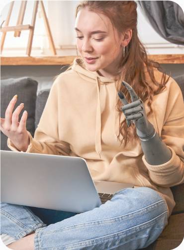 A woman with a prosthetic arm works on her laptop on the sofa.